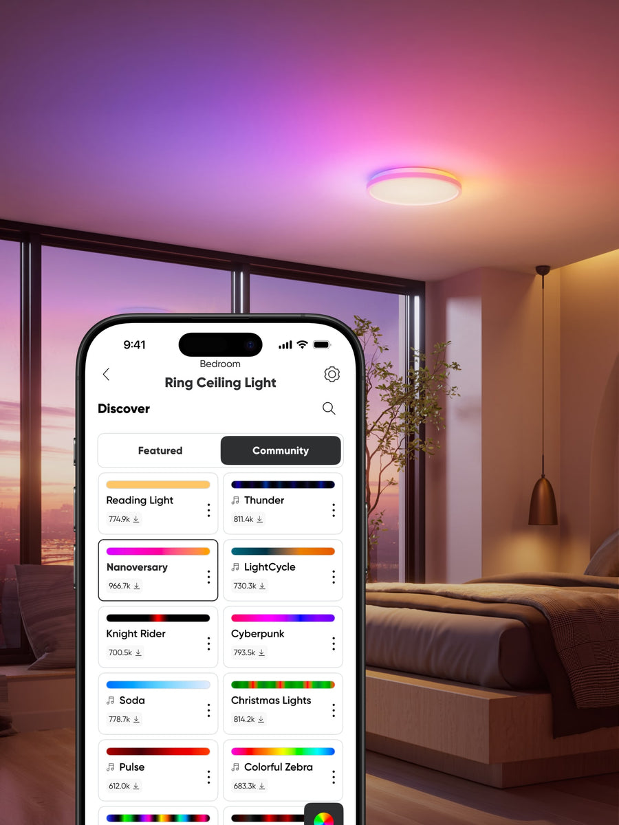 A smartphone displays a Ring app screen for a ceiling light in a modern bedroom setting. The phone is shown in the foreground, while the background features a glowing ceiling light emitting pink and purple light, with a bed and window visible.